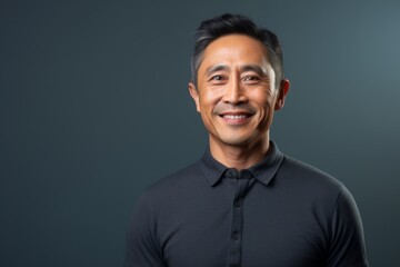 Fototapeta premium Portrait of a smiling asian man in his 50s showing off a lightweight base layer over minimalist or empty room background