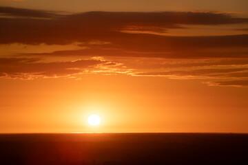 A radiant sunset over a forested horizon, with the sun casting a warm, golden glow across the sky and landscape. The vibrant orange and yellow hues create a stunning and tranquil scene. Copy space.