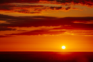 A radiant sunset over a forested horizon, with the sun casting a warm, golden glow across the sky and landscape. The vibrant orange and yellow hues create a stunning and tranquil scene. Copy space.