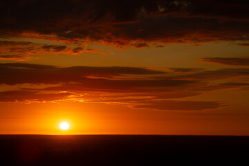 A radiant sunset over a forested horizon, with the sun casting a warm, golden glow across the sky and landscape. The vibrant orange and yellow hues create a stunning and tranquil scene. Copy space.