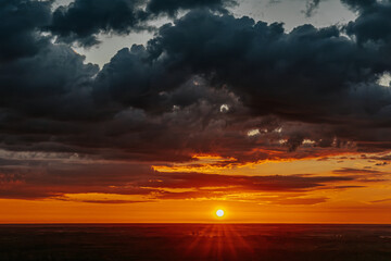 A breathtaking sunrise over the vast forest landscape with vibrant orange and yellow hues blending into the dark sky. Dramatic clouds add depth to the landscape. Copy space.