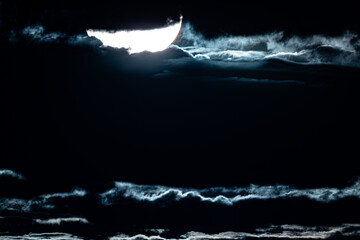 A striking night sky with the moon partially obscured by clouds, creating a dramatic and mysterious...