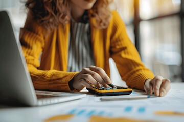 Fototapeta premium Businesswoman Using Calculator for Financial Report Analysis with Laptop and Growth Chart on Desk