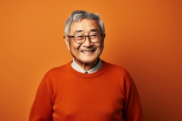 Obraz premium Portrait of a grinning asian elderly man in his 90s wearing a cozy sweater while standing against solid color backdrop