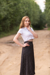 Portrait of a beautiful long-haired girl in a white T-shirt and black skirt in a city park.
