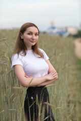 Portrait of a beautiful long-haired girl in a white T-shirt and black skirt in a city park.