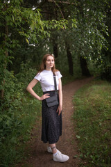 Portrait of a beautiful long-haired girl in a white T-shirt and black skirt in a city park.