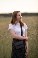 Portrait of a beautiful long-haired girl in a white T-shirt and black skirt in a city park.