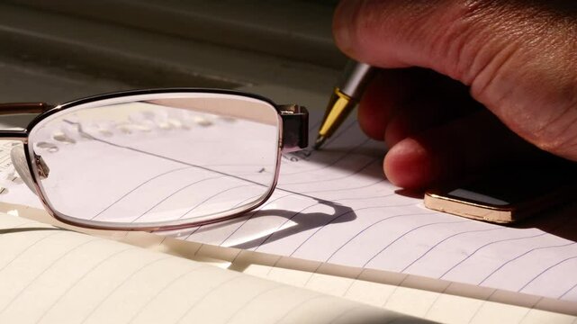 Reading glasses on notepad with hand making notes 
