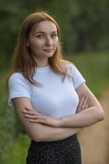 Portrait of a beautiful long-haired girl in a white T-shirt and black skirt in a city park.