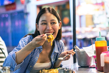 Young Asian woman traveler tourist eating Thai street food in China town night market in Bangkok in Thailand - people traveling enjoying food culture concept