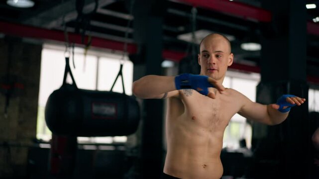 close-up in a boxing fight club bald young boxer with tattoos in blue bandages trains punches shadow boxing professional technique training