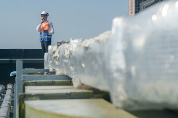 A male engineer works with communications on the roof of a tall building with surrounding engineering systems.