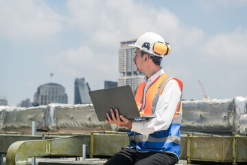 A male engineer works with communications on the roof of a tall building with surrounding engineering systems.