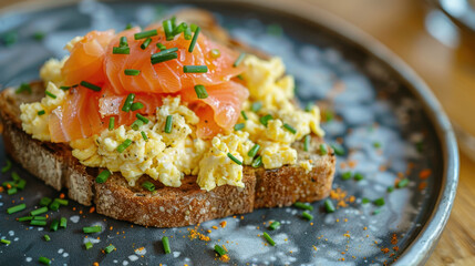 Close-up of smoked salmon and scrambled eggs on toasted whole grain bread garnished with chopped chives