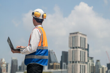 A male engineer works with communications on the roof of a tall building with surrounding...
