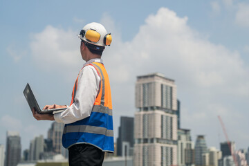 A male engineer works with communications on the roof of a tall building with surrounding...