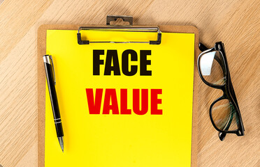 FACE VALUE text on yellow paper on clipboard with pen and glasses