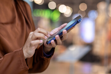 Close-up of hands interacting with a smartphone in a busy shopping mall. Background features colorful bokeh lights creating a lively, modern atmosphere, emphasizing connectivity, technology