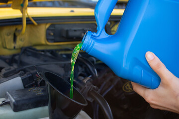 Pouring coolant antifreeze fluid into reservoir in vehicle engine using black funnel