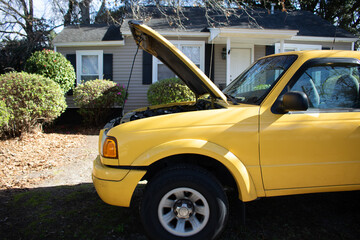 Side view of yellow pickup truck with hood up in front of home