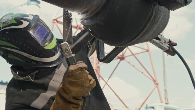 In this image, a worker dons full welding gear, focusing intently on welding a pipe amidst flying sparks. The setup reflects a workshop environment where precision and safety are paramount.