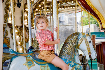 Fototapeta premium Happy positive preschool girl having a ride on the old vintage merry-go-round in city of St Malo France. Smiling child on a horse.