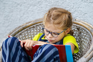 Little girl with eyeglasses reading book. Happy interested child learning.