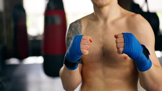 close-up in boxing fight club, a bald young boxer with tattoos in blue bandages stretches his hands before a fight professional training