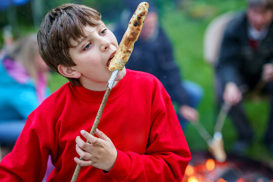 Teenager boy roasting bread stick on fire in teen camp in summer. Happy child spending vacations in sports camp.