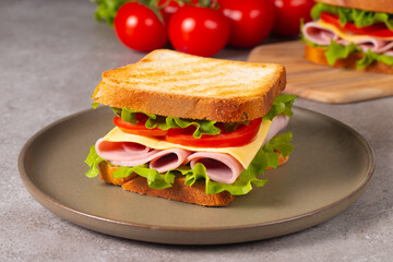Close-up of two sandwiches with bacon, salami, prosciutto and fresh vegetables on rustic wooden cutting board. Club sandwich concept