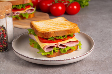 Close-up of two sandwiches with bacon, salami, prosciutto and fresh vegetables on rustic wooden cutting board. Club sandwich concept