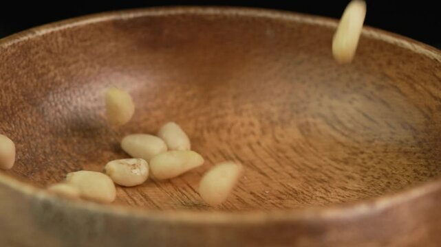 Peeled pine nuts are poured into a wooden bowl in slow motion. Pine nut kernels close up. Healthy nut