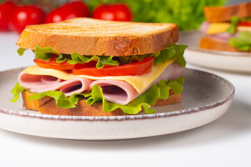 Close-up of two sandwiches with bacon, salami, prosciutto and fresh vegetables on rustic wooden cutting board. Club sandwich concept