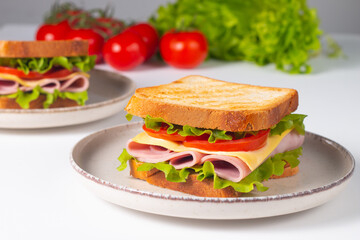 Close-up of two sandwiches with bacon, salami, prosciutto and fresh vegetables on rustic wooden cutting board. Club sandwich concept