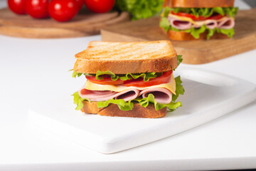 Close-up of two sandwiches with bacon, salami, prosciutto and fresh vegetables on rustic wooden cutting board. Club sandwich concept