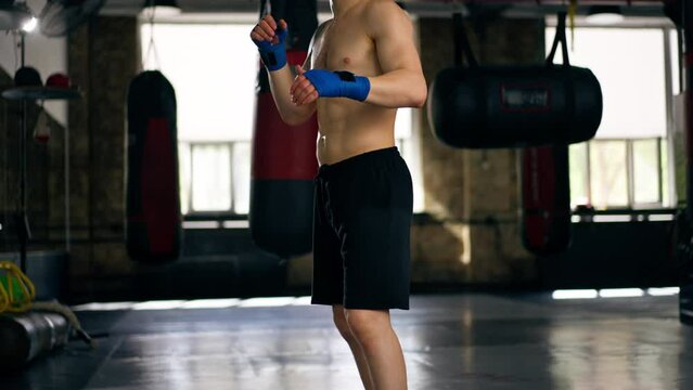 in a boxing fight club bald young boxer with tattoos in blue bandages trains a kick before a fight professional training fighting technique training