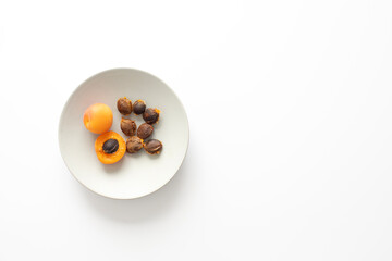 Top view of a light gray plate with ripe apricots and apricot stones on off white background with copy space