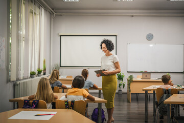 Mature teacher hold tablet and check how her students learn lesson