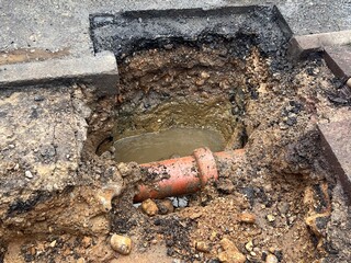 Close up of broken water pipe in construction site in the ground showing drains dug up on road with...