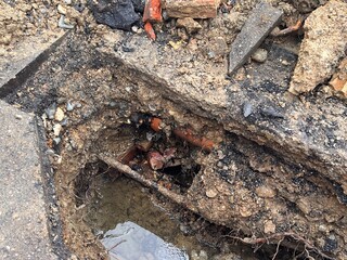 Close up of broken water pipe in construction site in the ground showing drains dug up on road with water works with earth rubble flooding bricks cement stone and soil in layers in urban city street