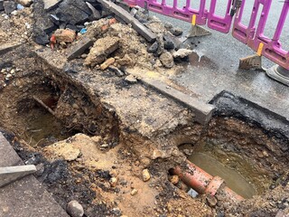 Close up of broken water pipe in construction site in the ground showing drains dug up on road with water works with earth rubble flooding bricks cement stone and soil in layers in urban city street