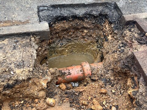 Close up of broken water pipe in construction site in the ground showing drains dug up on road with water works with earth rubble flooding bricks cement stone and soil in layers in urban city street