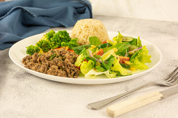 A plate of seasoned ground beef, steamed broccoli, carrots, brown rice, and a fresh, crisp salad.