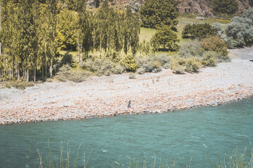 A lonely Afghan walks along the bank of the Panj River with blue water