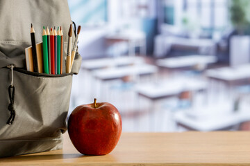 Back to school concept. Wooden desk top with backpack and apple and school stuff with blurred...