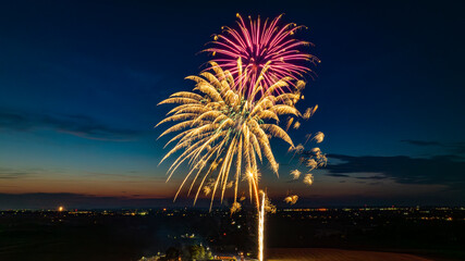 Golden And Pink Fireworks Exploding In The Night Sky, Creating Brilliant Bursts Over The Distant Cityscape And A Gathered Crowd, With The Vibrant Twilight Horizon Enhancing The Festive Atmosphere.