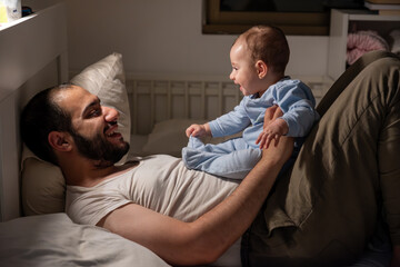 Father takes care of his newborn while can't sleep in night on bed with dim yellow light, hard to...