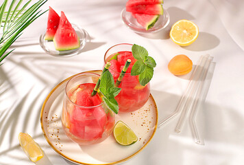 Ice cold homemade lemonade or cocktail with mint, watermelon and fruit, a recipe for a refreshing summer drink. Two glasses with fruit drink on sunny table, detox diet and weight loss concept, 