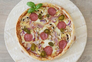 Whole Homemade Pizza with Salami or Pepperoni on Wooden Table with Ingredients Background. National Pizza Day, La Giornata Mondiale della Pizza, World Pizza Day. Tasty, Food, Fast Food, Hunger.